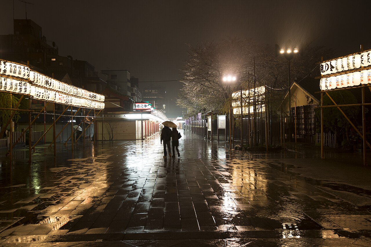 Lanterns reflected on rain-wet Nakamise-dōri, with closed shops and two people under umbrellas